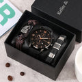 A men's wristwatch gift set in an open black presentation box, featuring a black leather strap chronograph watch with a black dial, a brown leather bracelet with a wolf emblem, and a black-and-silver textured bangle. 