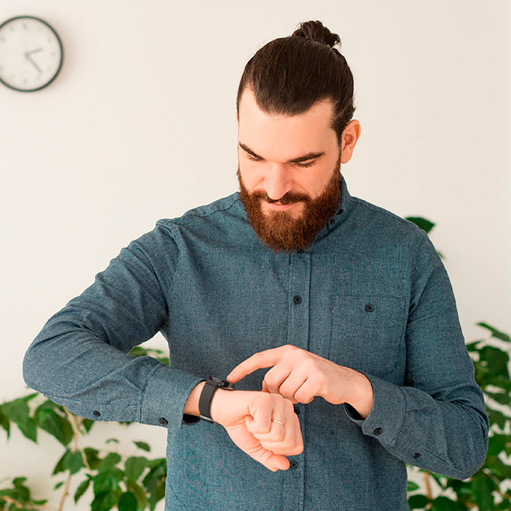 Man in a blue shirt checking his watch against a light background with plants.